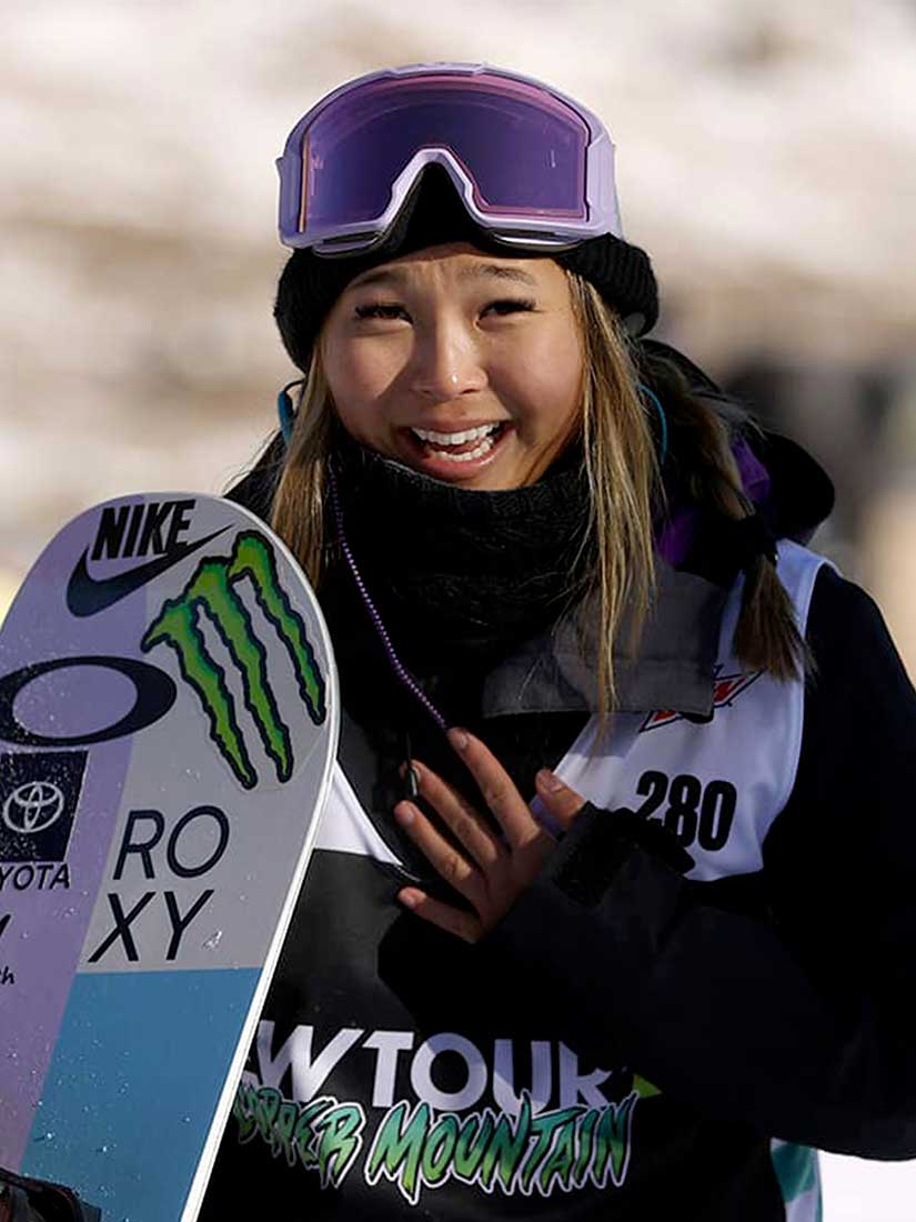 Athlète souriant après une compétition de snowboard demi-lune et portant un dossard de compétition.