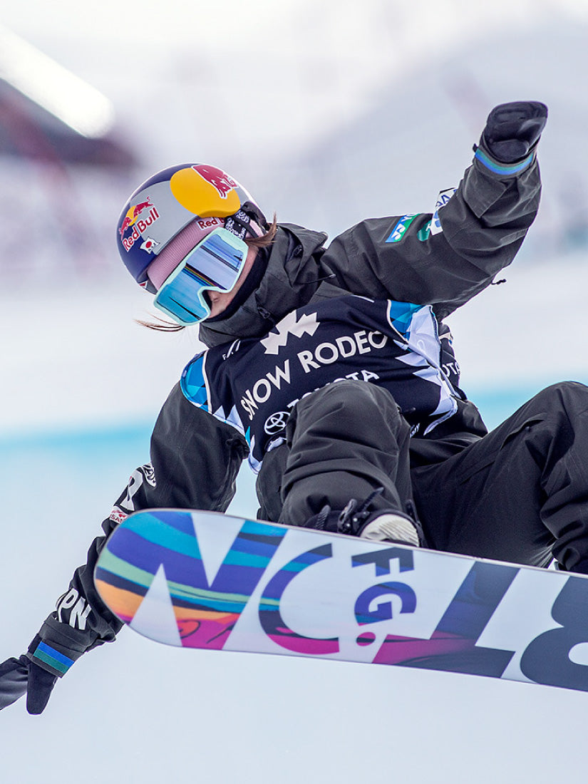 Athlète pratiquant une acrobatie avec une planche à neige et portant un dossard de compétition demi-lune imprimé.