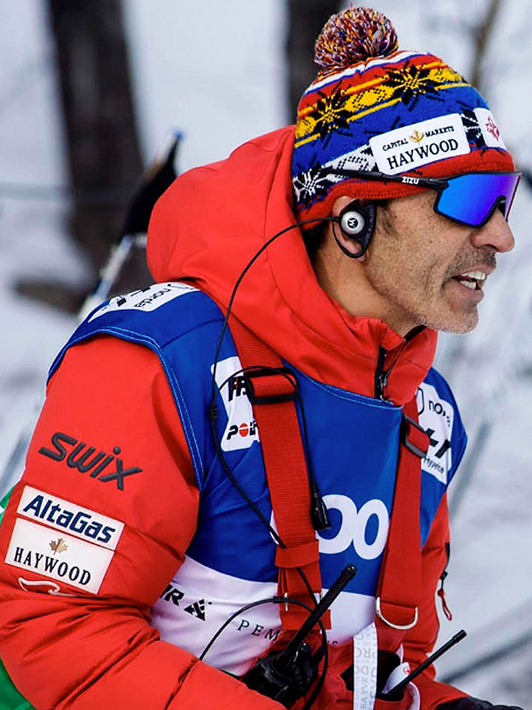 Entraîneur de ski coachant ses athlètes et portant un dossard imprimé pour l'identifier.